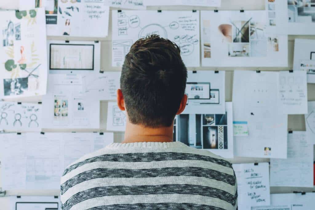 Back view of man looking at the research paper pinned at the wall