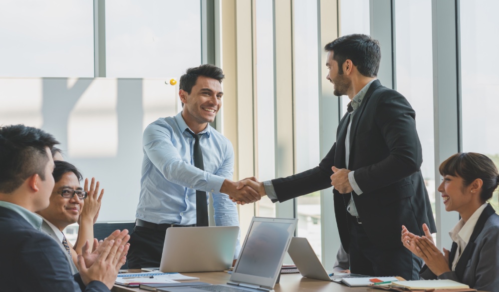 2 professional shaking hands while others clap