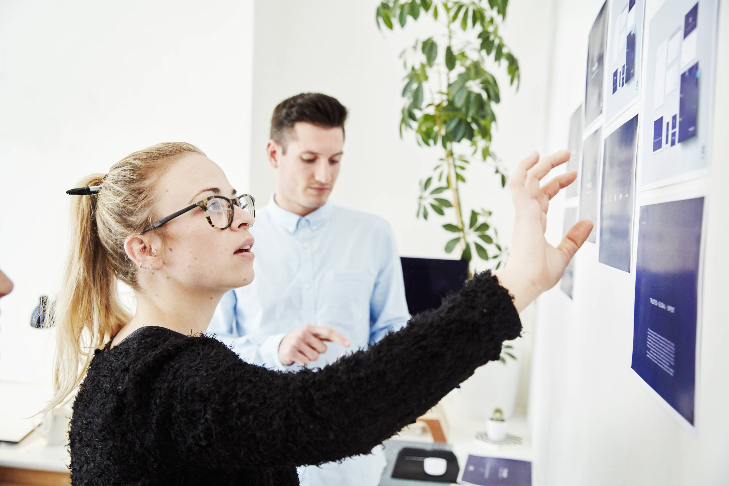 Two designers looking at printed plans stuck on a wall
