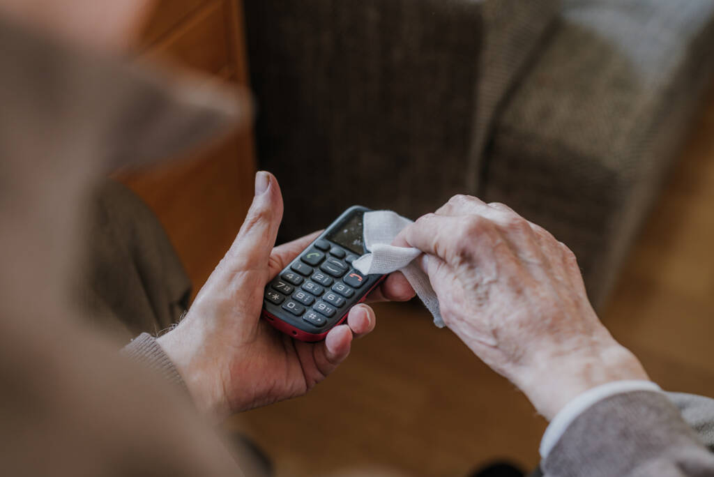 An old person cleaning a phone with keypad