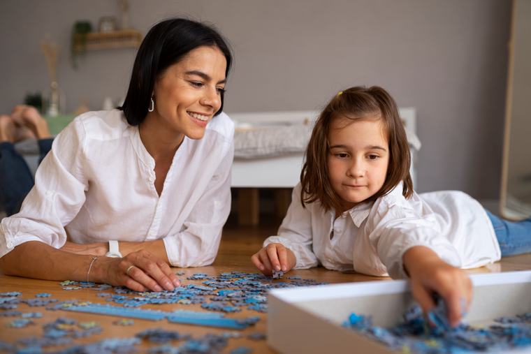 Smiling lady with her daughter playing with puzzle