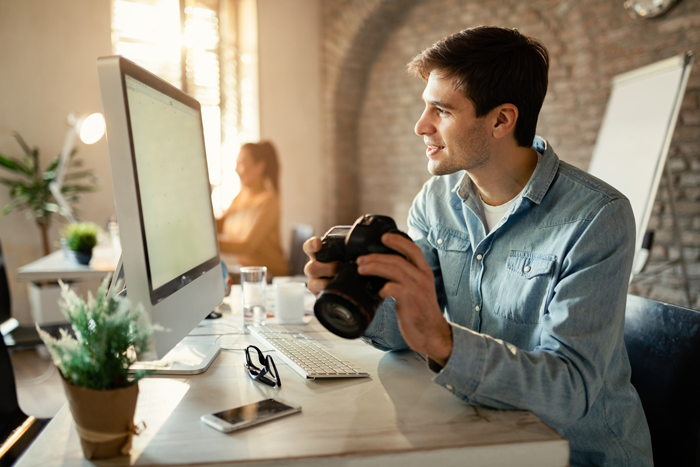 Smiling man looking at computer while having camera in his hand