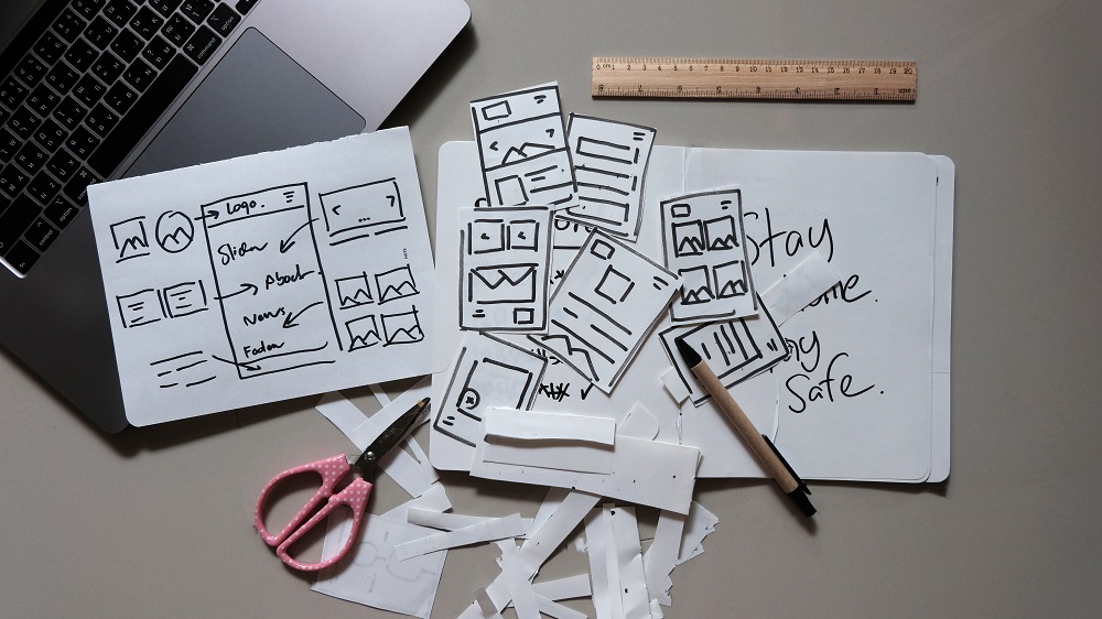 Wireframe messy skeych on paper laid out next to a laptop for planning UX design