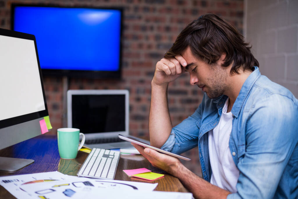 Stressed businessman holding digital tablet in creative office
