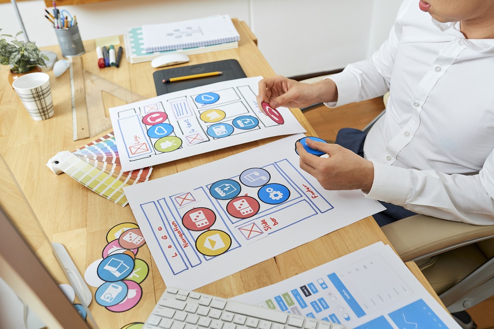 Web designer planning mobile application by spreading out paper icons