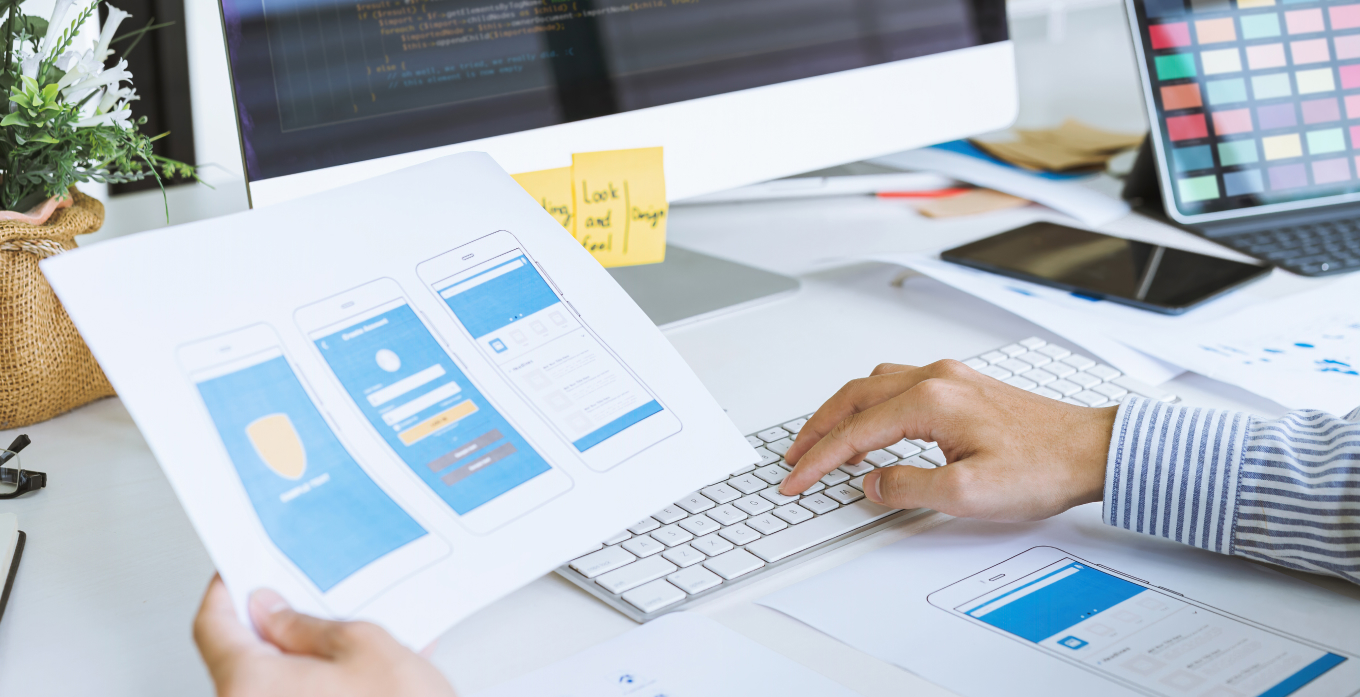 Man working on codes while looking at the mobile ui screen on paper sheet