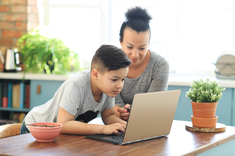 Boy browsing laptop while her mother looking him from side