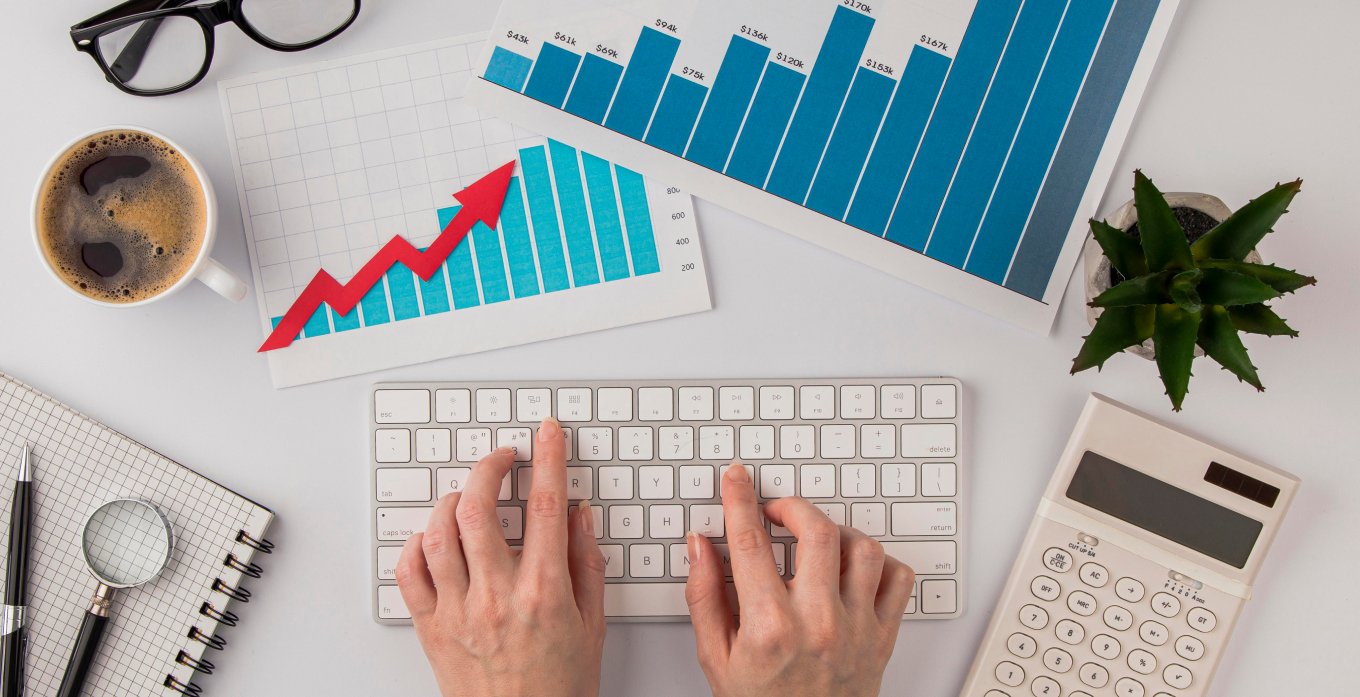 someone is typing on keyboard with coffee, data sheets and calculator on desk